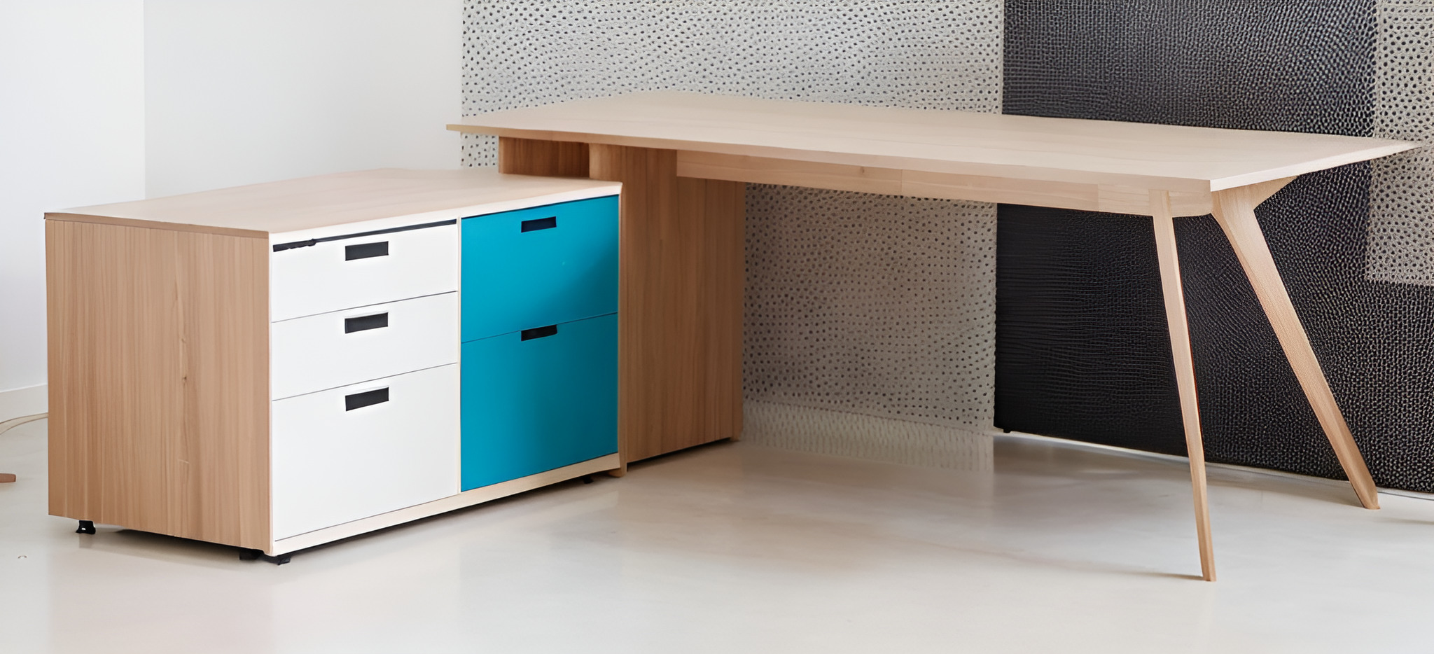 Jasne biurko z drewna z nogami w stylu skandynawskim i kontenerkiem z szufladami w kolorach bieli i turkusu na kółkach, na tle ściany z wzorem.