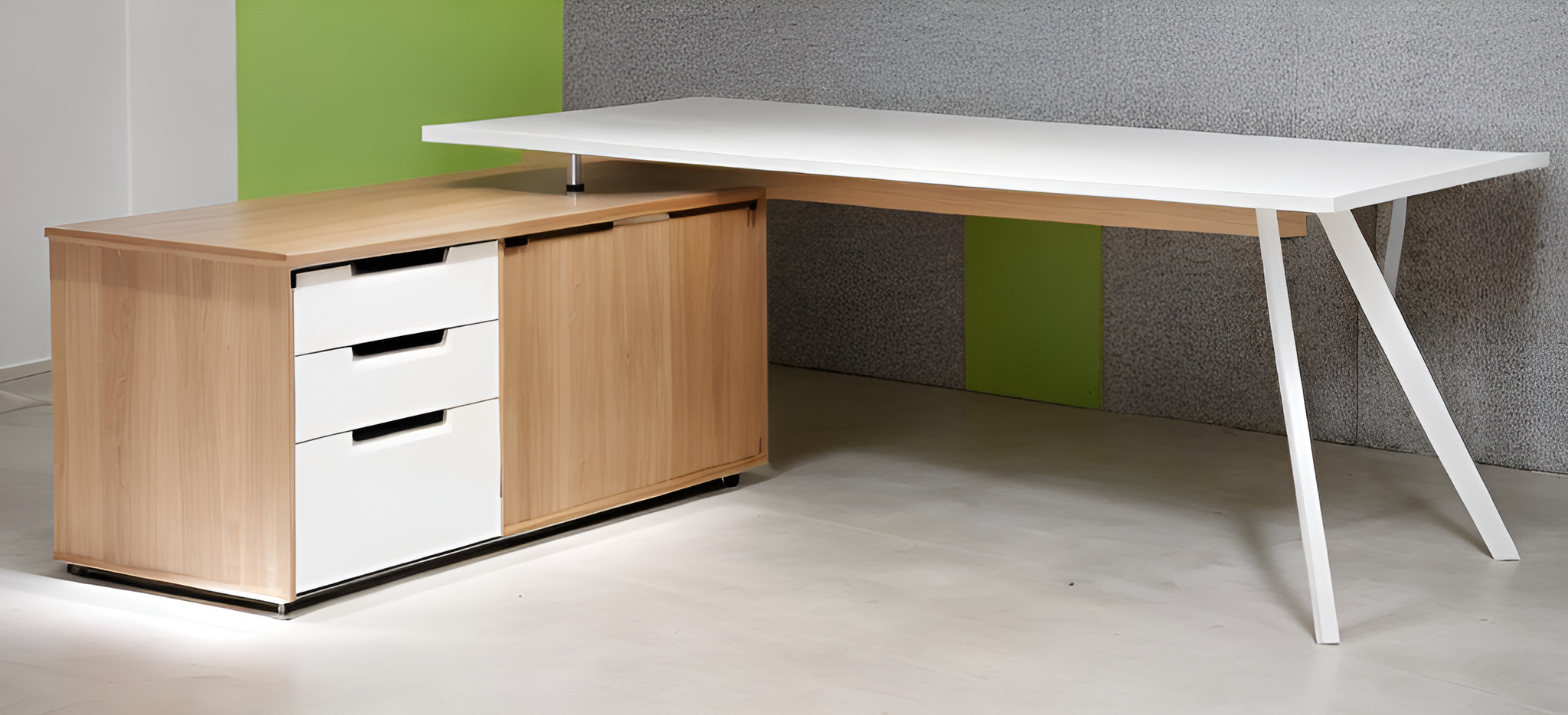 Nowoczesne biurko z blatem w kolorze białym, wspartym na białych, skośnych nogach, połączone z drewnianym kontenerem z trzema białymi szufladami i zamykaną szafką, na tle szaro-zielonej ściany.