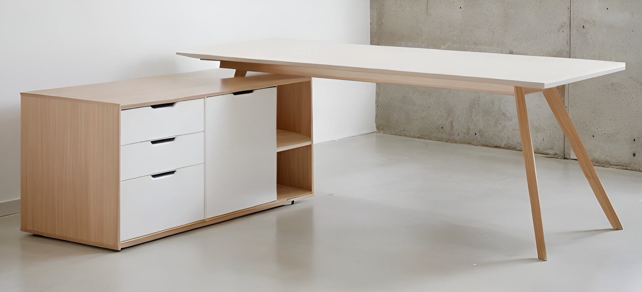 Nowoczesne biurko narożne z jasnego drewna i białymi frontami szuflad, minimalistyczny design, widoczne trzy szuflady i otwarte półki, na betonowym tle.