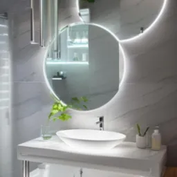 Nowoczesna łazienka z okrągłymi lustrami podświetlanymi LED, białą umywalką nablatową, marmurowymi płytkami i elementami dekoracyjnymi z zielonych roślin.