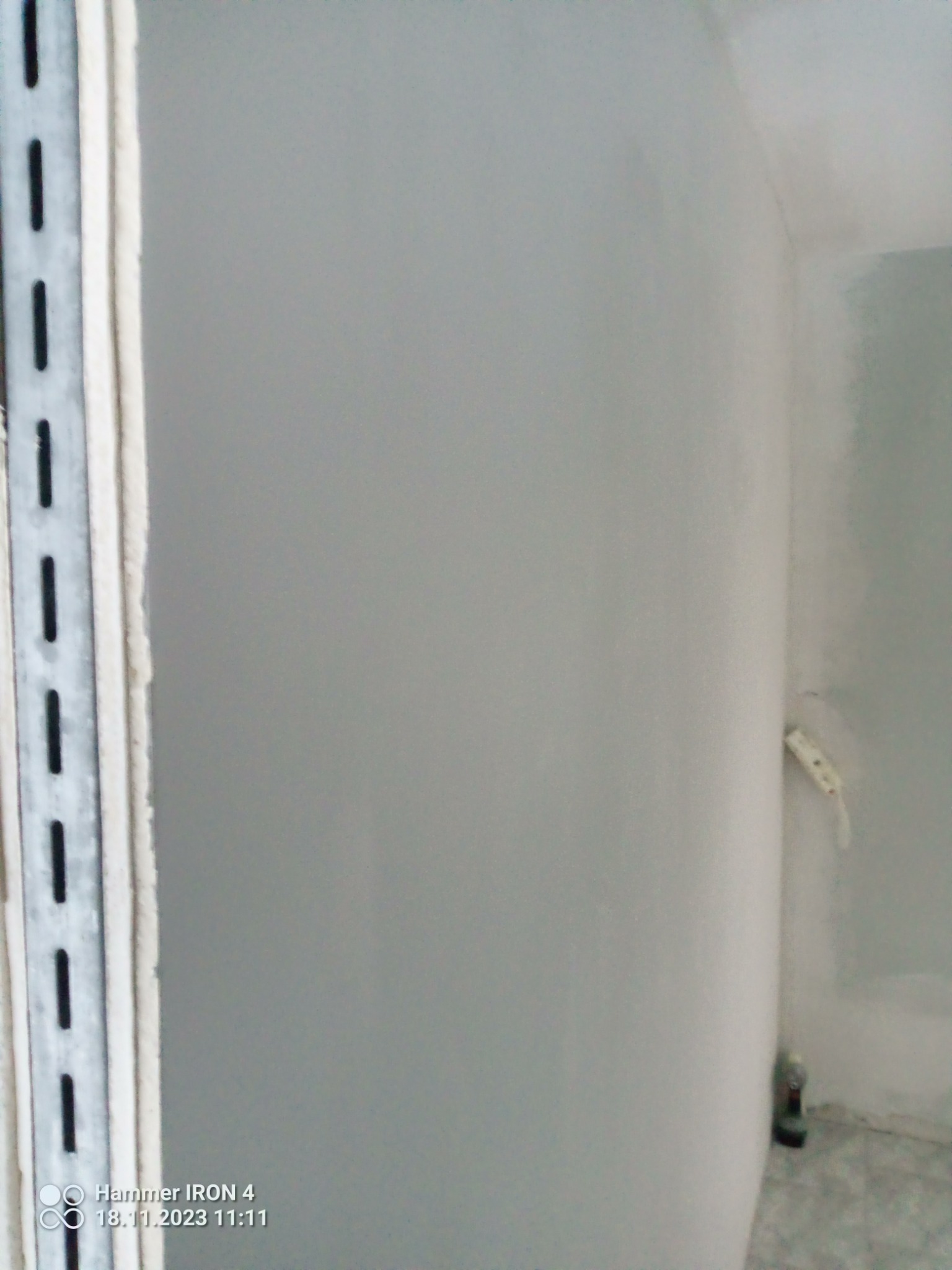 Świeżo wyszpachlowana ściana z metalowym profilem pionowym po lewej stronie, widoczne nierówności i niedoskonałości wymagające dalszej obróbki.