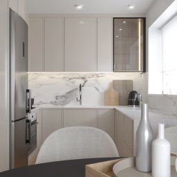 Daniela Beker Projektowanie Wnętrz - Jasna kuchnia w stylu minimalistycznym z marmurowym blatem, zabudową meblową pod sufit, złotymi uchwytami i srebrną lodówką; na stole dekoracyjne butelki i szklany wazon z suchymi gałązkami.