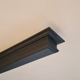 Vielkibud Oleksandr Kulbakov - Ciemna, profilowana listwa przysufitowa po malowaniu, kontrastująca z jasnym sufitem, widok z dołu, oświetlenie naturalne.