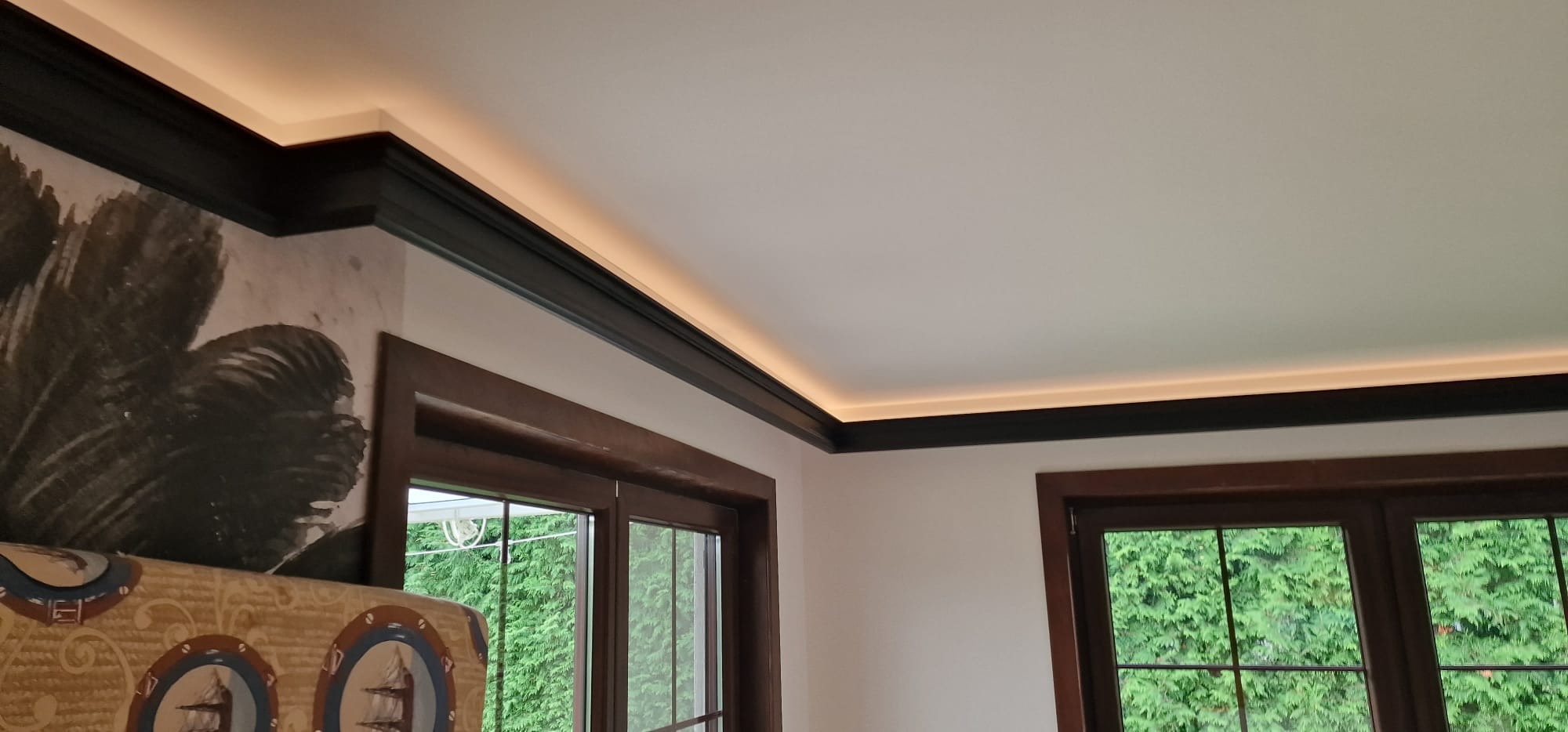 Pokój po renowacji z dwoma oknami w drewnianych ramach, czarną listwą przysufitową z ukrytym oświetleniem LED oraz fragmentem ściany z dekoracyjną tapetą w stylu vintage z motywem roślinnym.