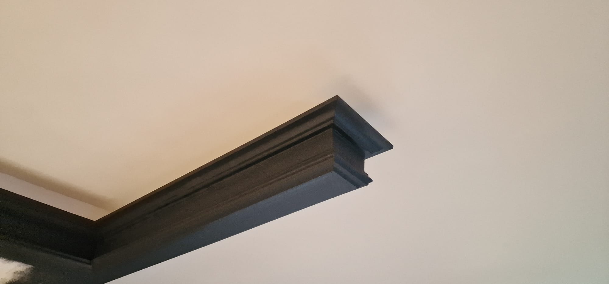 Ciemna, profilowana listwa przysufitowa po malowaniu, kontrastująca z jasnym sufitem, widok z dołu, oświetlenie naturalne.