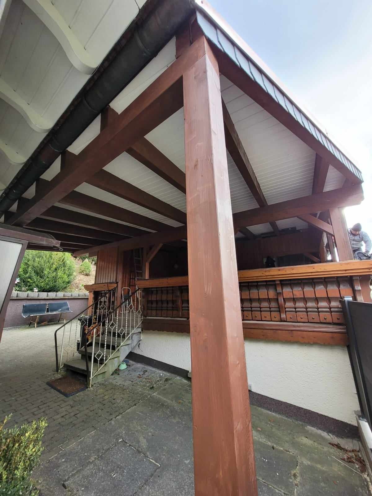 Drewniana konstrukcja z białym podsufitkiem i metalową rynną, widoczny fragment dachu z blachy oraz pracownik na górze.