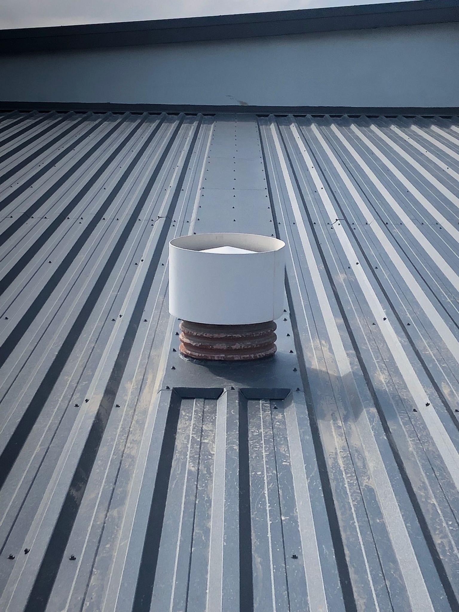 Szary dach z blachy trapezowej z kominkiem wentylacyjnym z tworzywa sztucznego i obróbką blacharską, widok z góry.