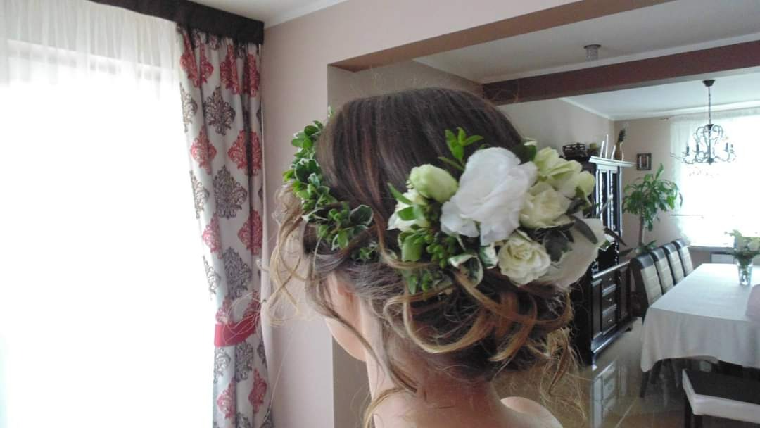 Upięcie ślubne z białych róż i zielonych liści, widok z tyłu, w tle okno z wzorzystymi zasłonami i fragment jadalni