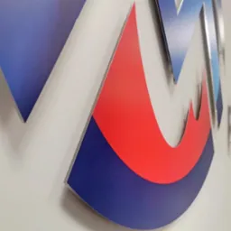 Trójwymiarowe logo firmy w kolorach czerwonym i niebieskim, zamontowane na białej ścianie biura, widoczne pod kątem.