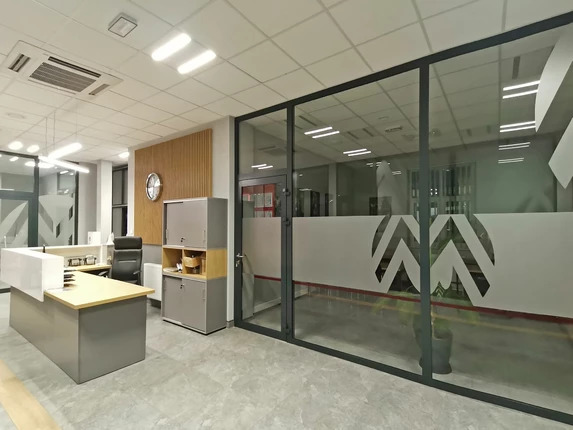 Nowoczesne biuro z recepcją, przeszklonymi ścianami z dekoracyjnym wzorem i szarą podłogą.