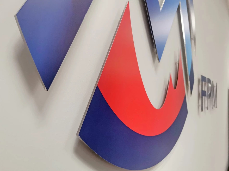 Trójwymiarowe logo firmy w kolorach czerwonym i niebieskim, zamontowane na białej ścianie biura, widoczne pod kątem.