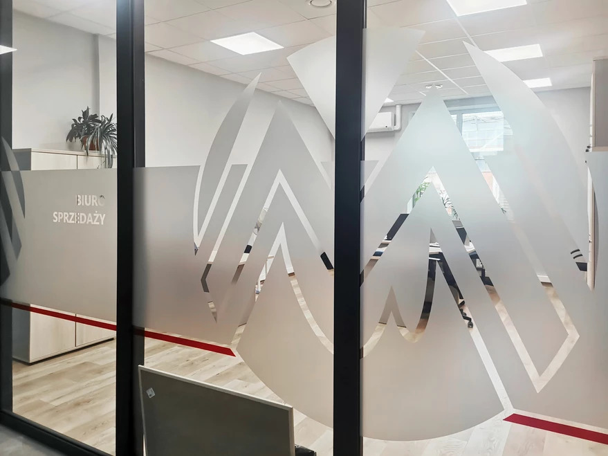 Oklejona szkłem grafika w biurze sprzedaży, z widocznym napisem 'Biuro Sprzedaży' na ścianie i elementami dekoracyjnymi na szybie.