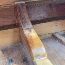 Surowe drewno z widocznymi śladami obróbki, niedoskonałościami i pyłem, prawdopodobnie w trakcie renowacji lub budowy konstrukcji drewnianej.