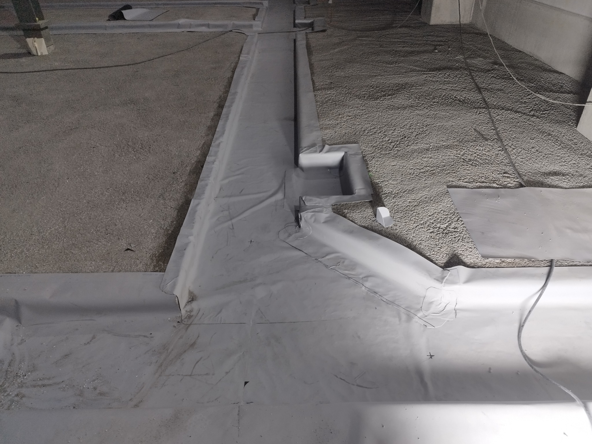 Przygotowanie podłoża pod wylewkę izolacyjną: rozłożona folia hydroizolacyjna z zaznaczonymi punktami na powierzchni, widoczny fragment ściany i warstwa izolacyjna z granulatu.