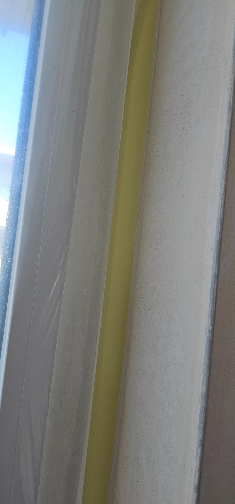 Okno zabezpieczone folią malarską i taśmą malarską przed malowaniem ściany o szorstkiej fakturze.