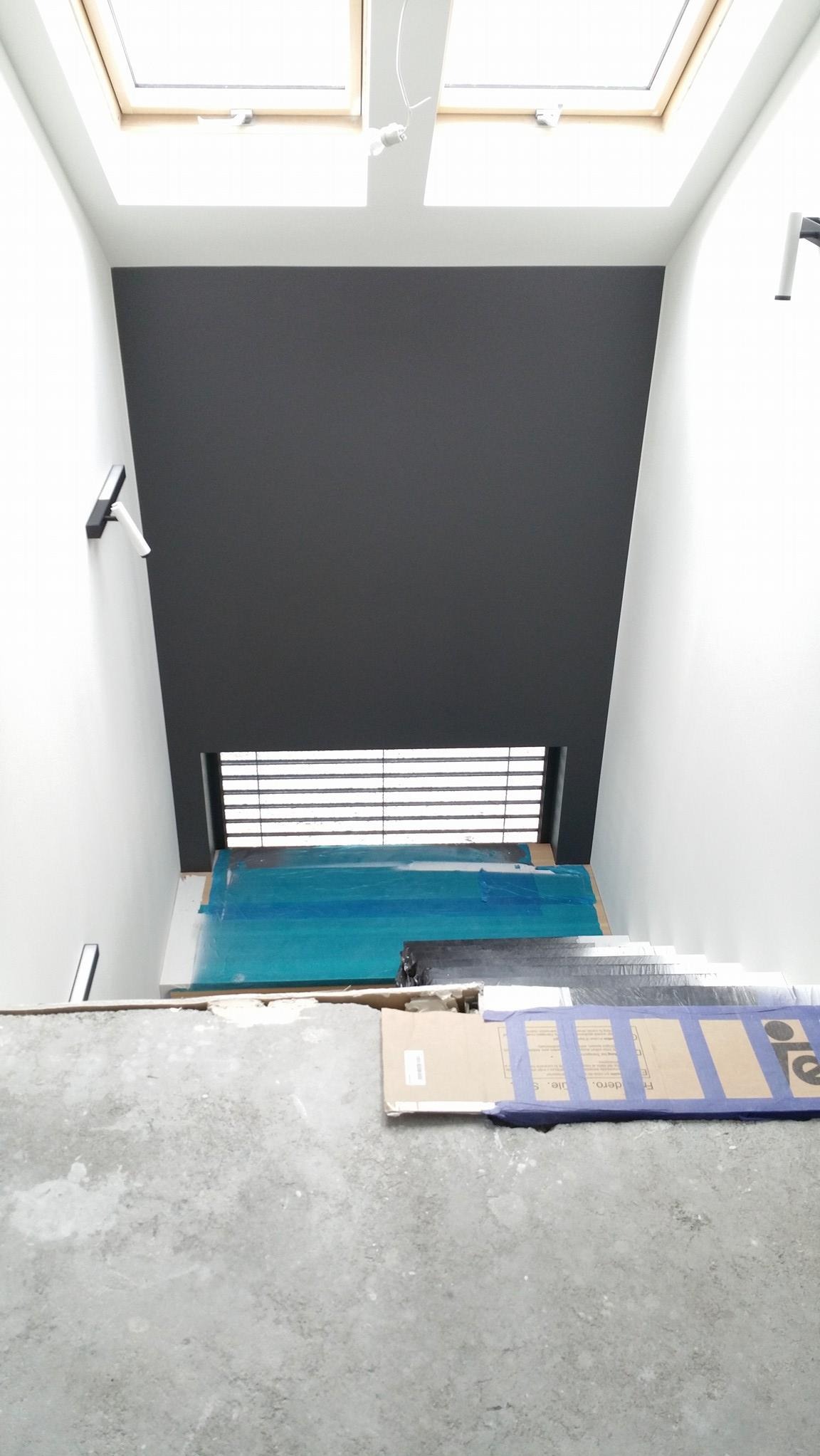 Wnętrze w trakcie prac w Warszawie: ściana pomalowana na ciemny szary kolor pod oknem dachowym, podłoga zabezpieczona folią i kartonem, widoczne ślady po remoncie.
