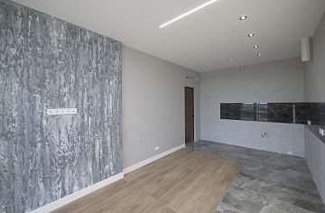 Wnętrze pomieszczenia z częściowo wykończonymi ścianami: jedna ściana pokryta dekoracyjną szarą strukturą przypominającą marmur z widocznymi gniazdkami elektrycznymi, pozostałe ściany pomalowane...