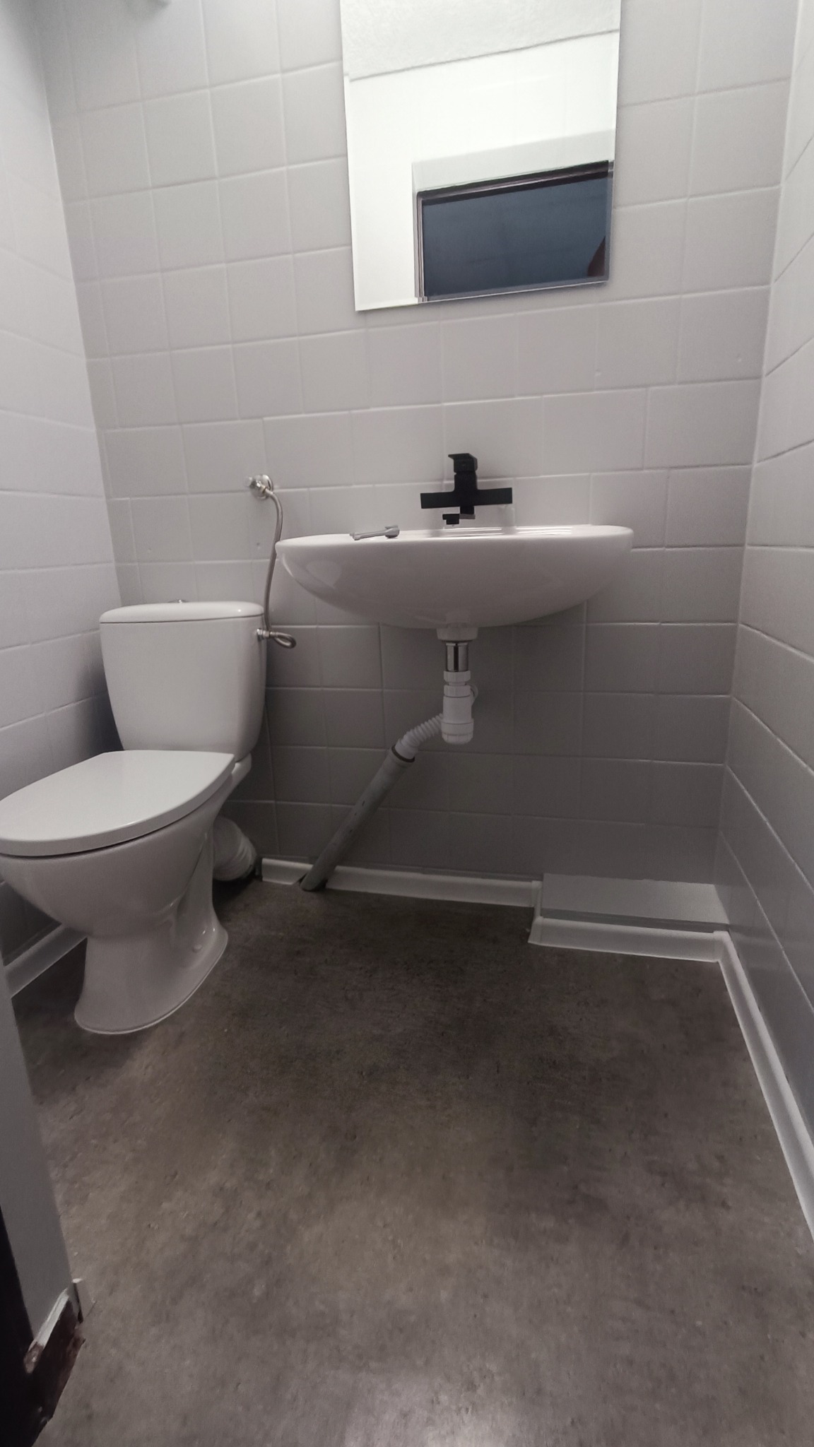 Wyremontowana łazienka w odcieniach szarości i bieli, z wiszącą umywalką z czarną armaturą, toaletą oraz lustrem nad umywalką.