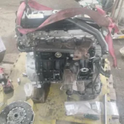 Silnik samochodowy zawieszony na pasach w warsztacie w Zabrzu, obok leży sprzęgło i narzędzia.