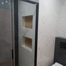 Emi Stan - Nowoczesna łazienka z kabiną prysznicową, biało-szare płytki imitujące marmur, wnęki z drewnianym wykończeniem, podwieszana toaleta z czarnym panelem sterującym.