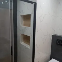 Nowoczesna łazienka z kabiną prysznicową, biało-szare płytki imitujące marmur, wnęki z drewnianym wykończeniem, podwieszana toaleta z czarnym panelem sterującym.