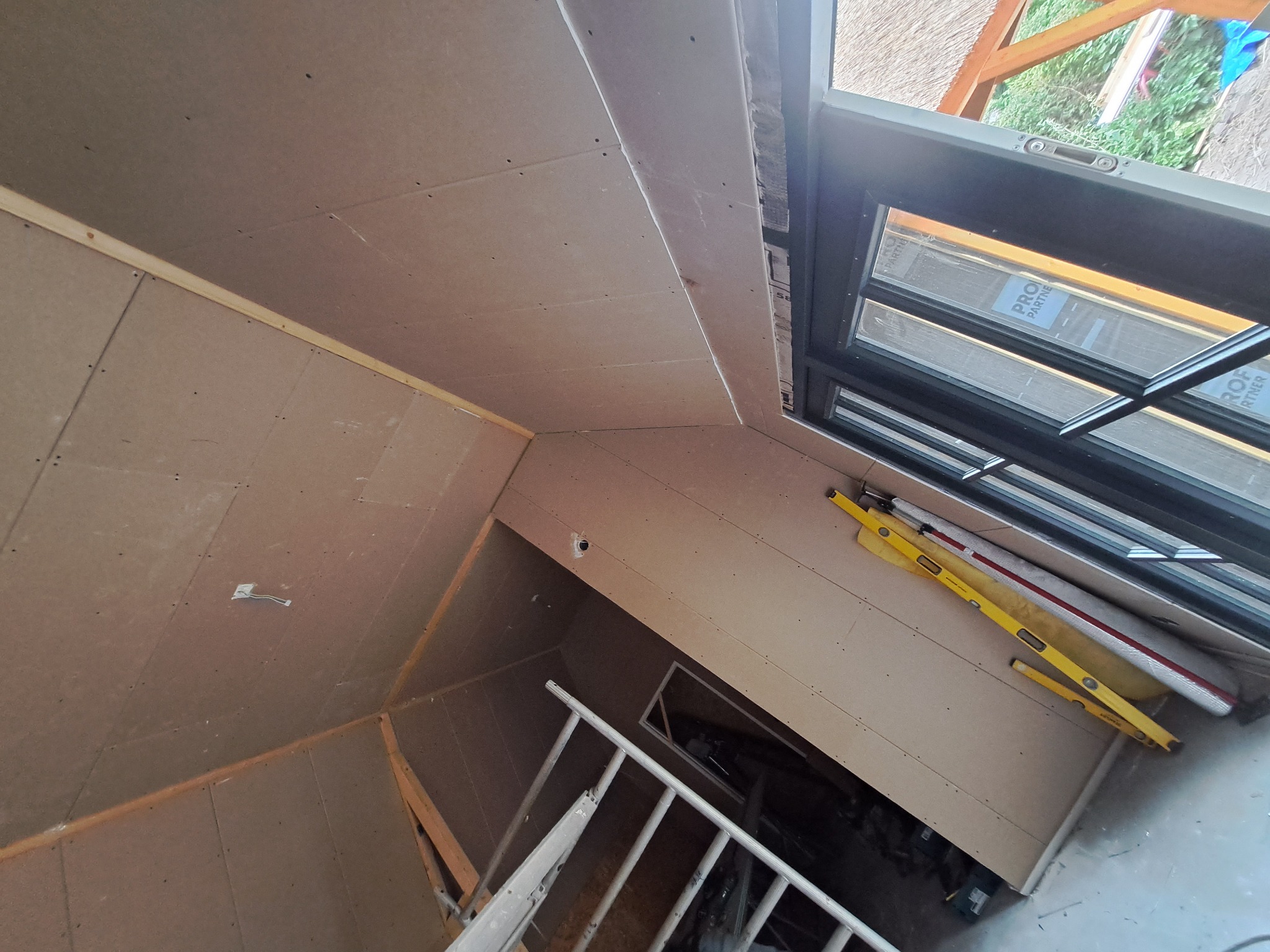 Montaż płyty gipsowo-kartonowej na poddaszu, widoczna drabina, poziomice i okno dachowe