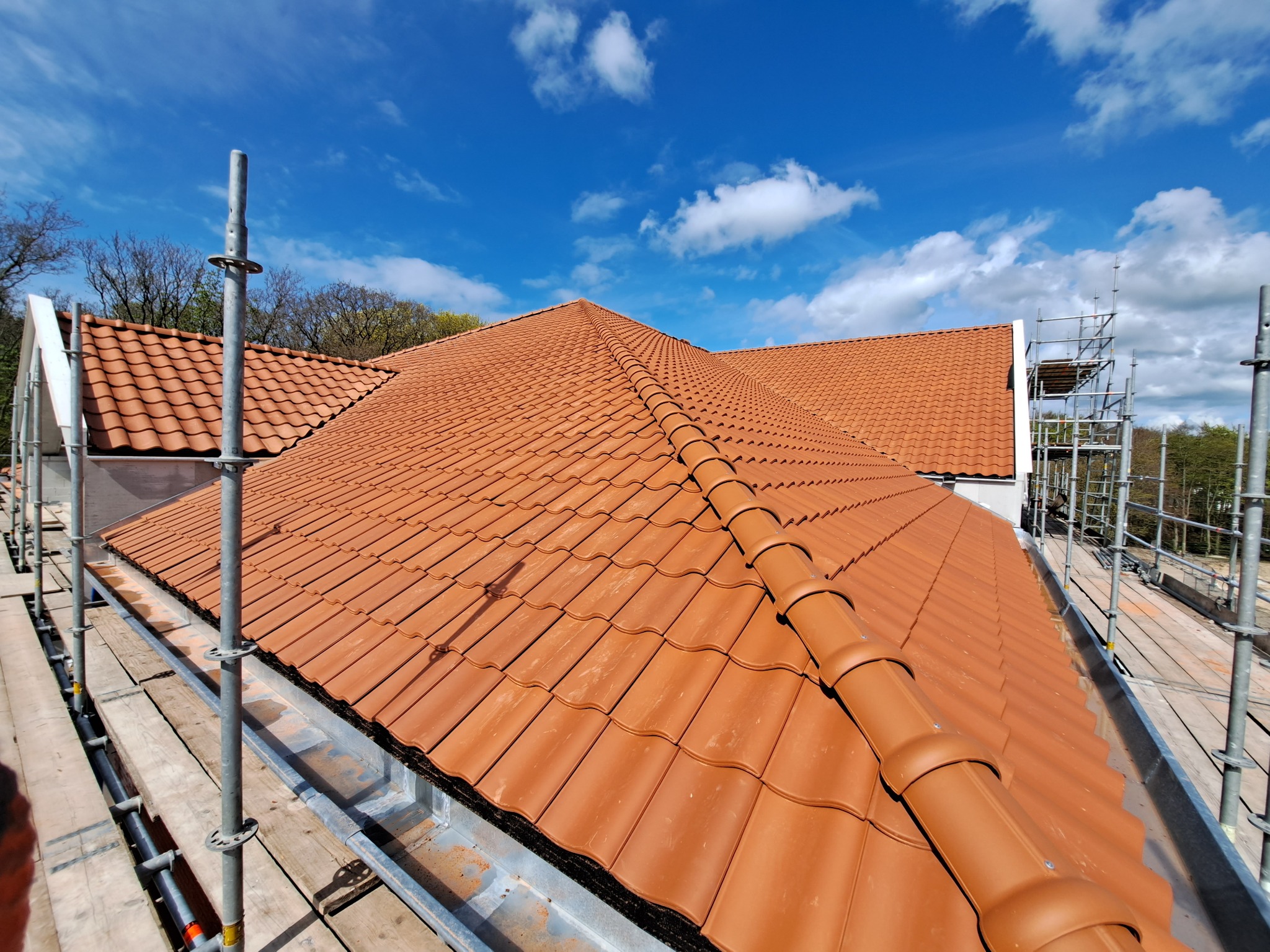 Nowy dach z czerwonej dachówki ceramicznej widziany z rusztowania, błękitne niebo w tle.