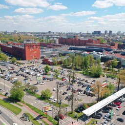Krzysztof Siwa Nodal Point - Panorama Łodzi z lotu ptaka, widok na budynek Manufaktury i parking, w tle zabudowa miejska i błękitne niebo z chmurami.