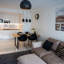 Krzysztof Siwa Nodal Point - Jasne, nowoczesne wnętrze mieszkania we Wrocławiu z otwartą kuchnią, jadalnią i salonem. Na ścianie dekoracyjne obrazy z motywami architektonicznymi.