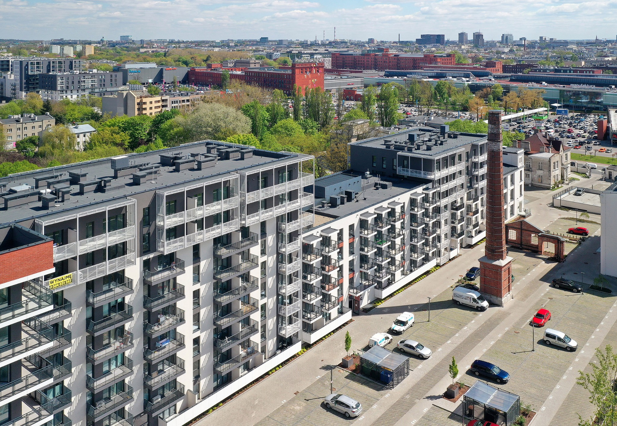 Wysoki kąt widzenia na nowoczesne budynki mieszkalne z balkonami, z ceglanym kominem w tle i widokiem na miasto.