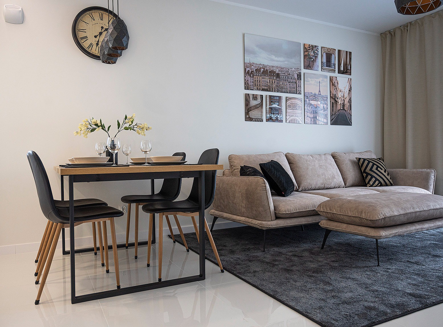 Jasne wnętrze mieszkania z drewnianym stołem, czarnymi krzesłami, beżową sofą i dekoracjami ściennymi z motywami Paryża.