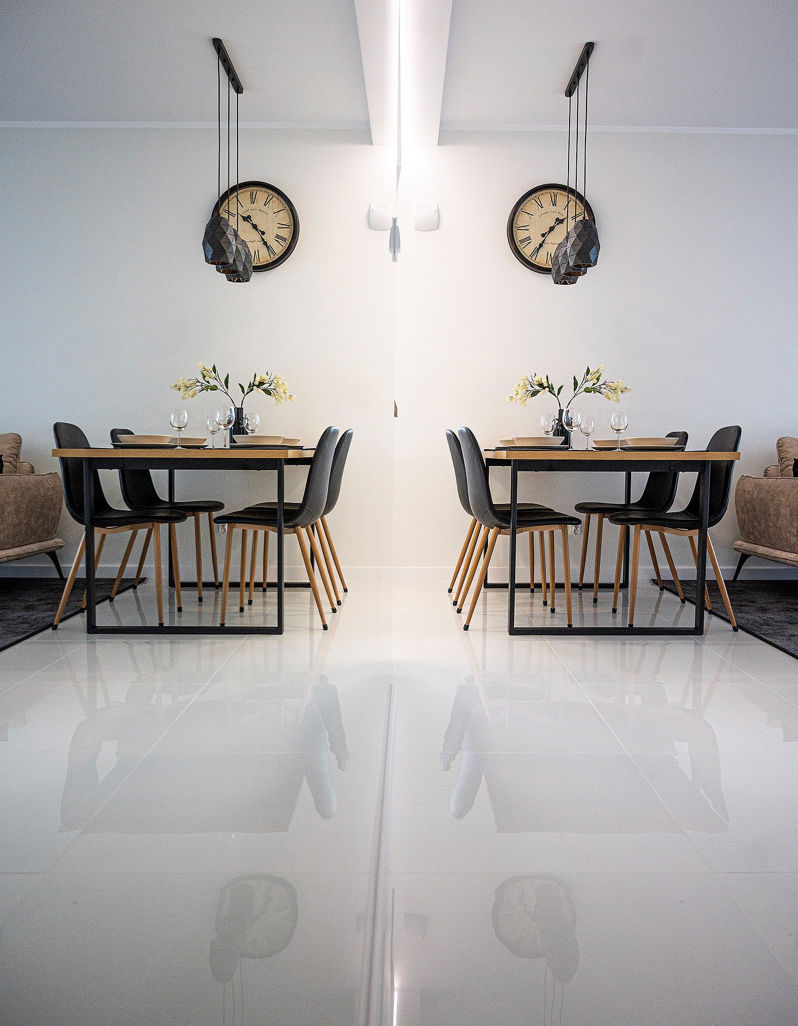 Minimalistyczna jadalnia z drewnianym stołem, czarnymi krzesłami i szklanymi naczyniami, odbicie w błyszczącej podłodze, zegary ścienne z geometrycznymi lampami.