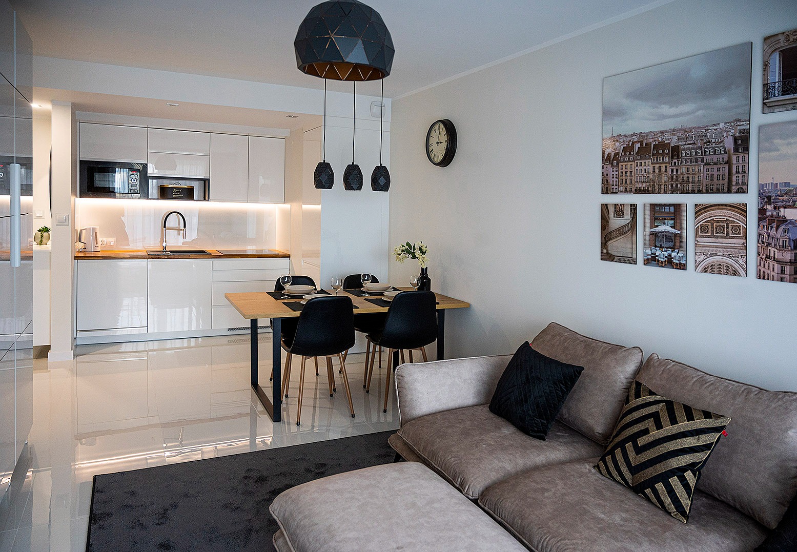 Jasne, nowoczesne wnętrze mieszkania we Wrocławiu z otwartą kuchnią, jadalnią i salonem. Na ścianie dekoracyjne obrazy z motywami architektonicznymi.