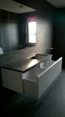 Nowoczesna łazienka z szarą płytką, białą szafką pod umywalką z wysuwanymi szufladami i ciemnym blatem.