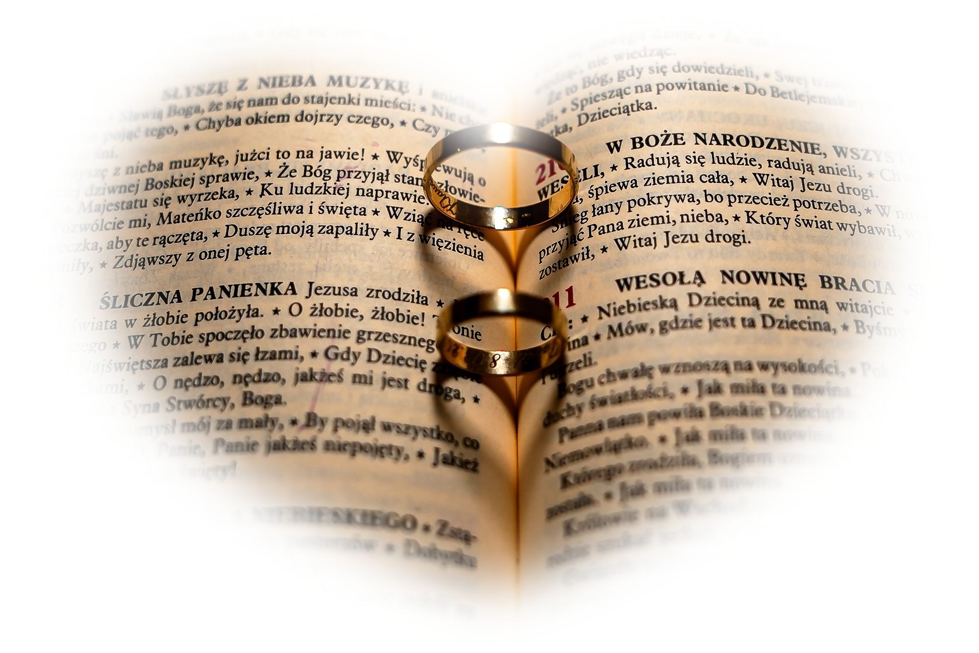 Dwa złote pierścionki ślubne leżące na otwartej książce z tekstami religijnymi, rzucające cień w kształcie serca.