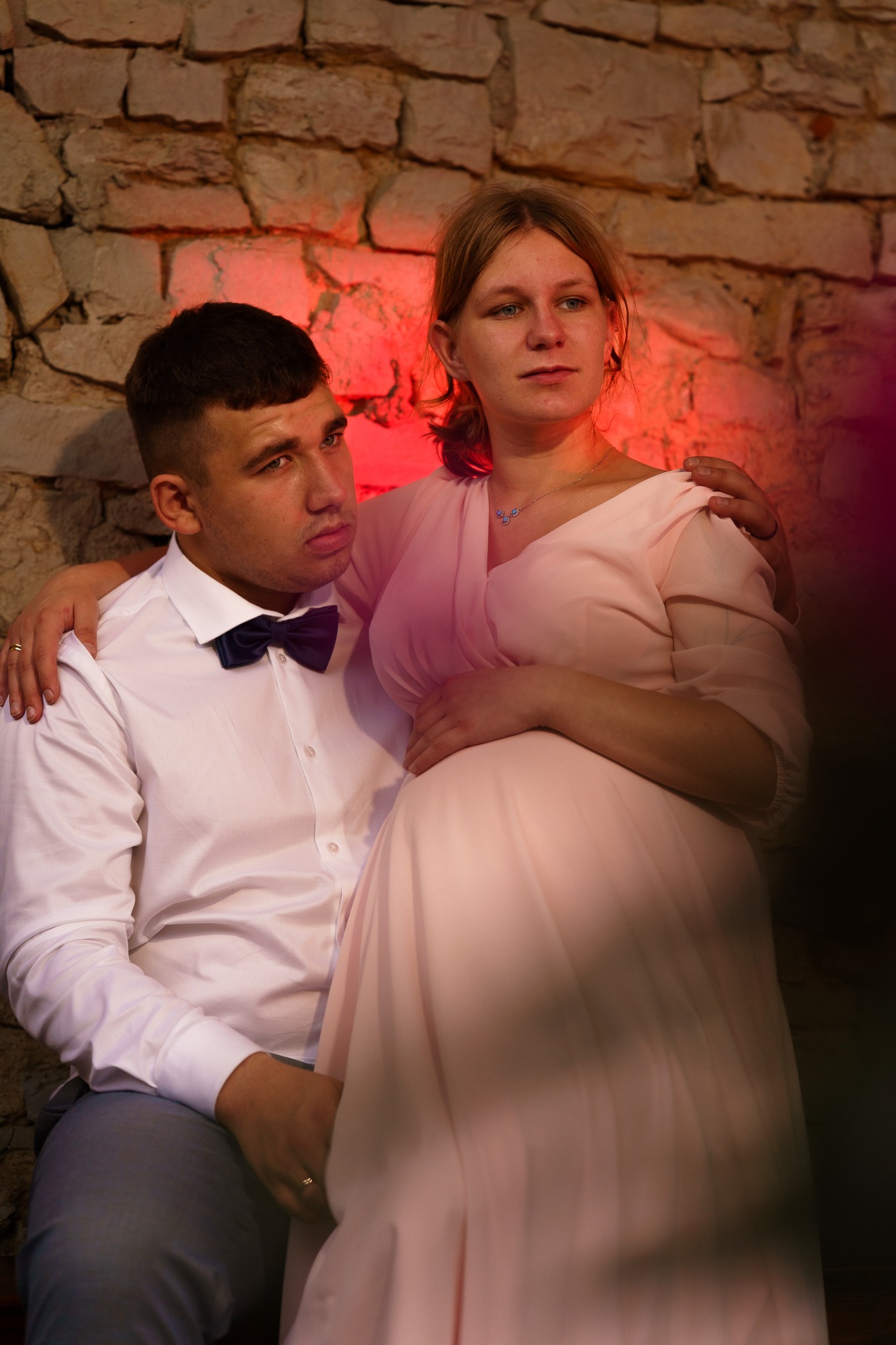 Ciąża w obiektywie: elegancka sesja w kamiennym wnętrzu. Przyszła mama w pudrowej sukni, czuły partner w muszce, romantyczny nastrój, delikatne światło.