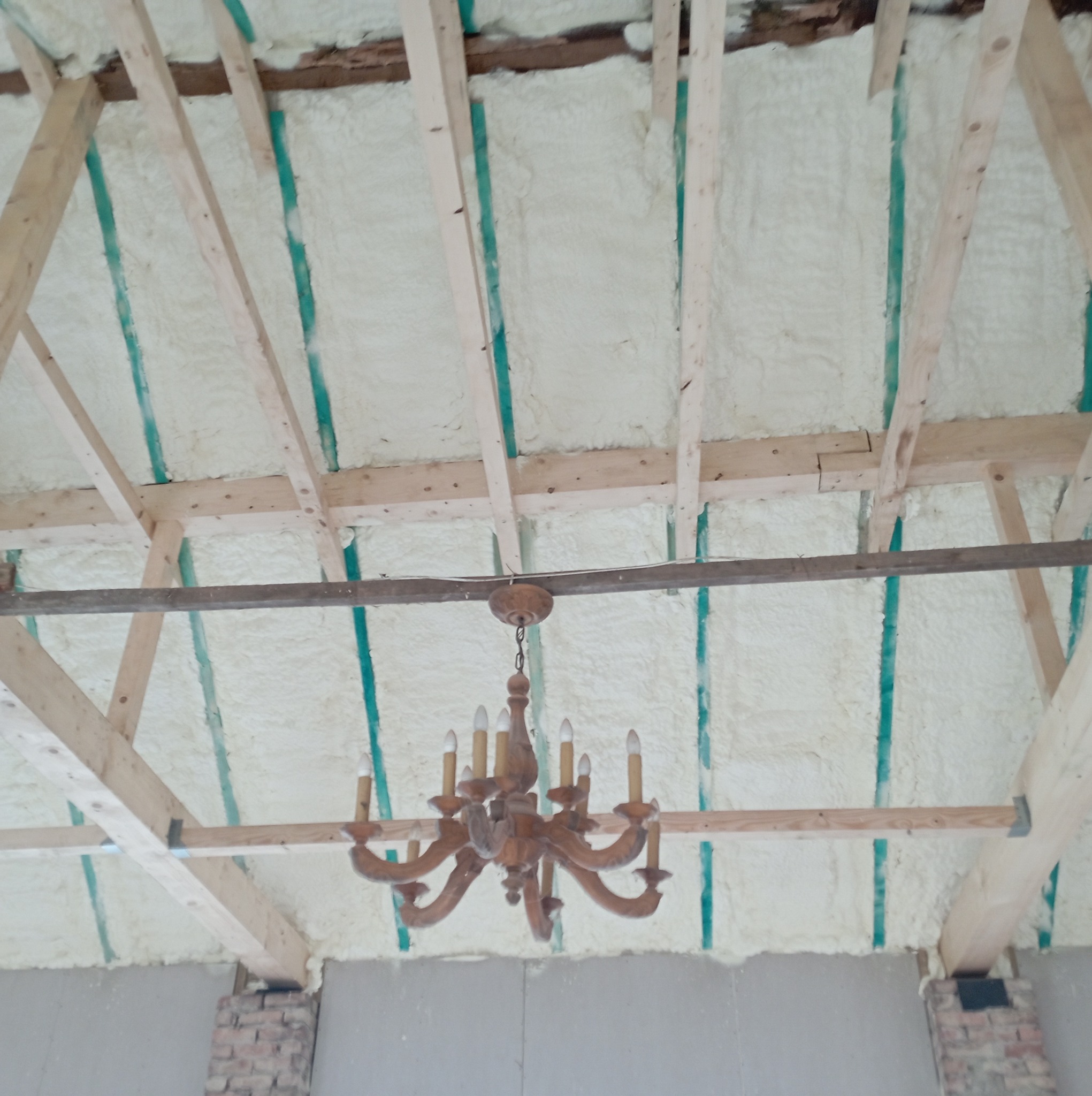 Poddasze z drewnianą konstrukcją dachu i wypełnioną pianką izolacyjną, widoczny fragment starego żyrandola.