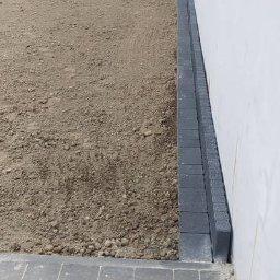 MICHAŁ GALAS GALASBRUK - Przygotowanie terenu pod przyszłą nawierzchnię w Krakowie, z widocznymi obrzeżami z kostki betonowej i fragmentem ułożonej kostki brukowej.