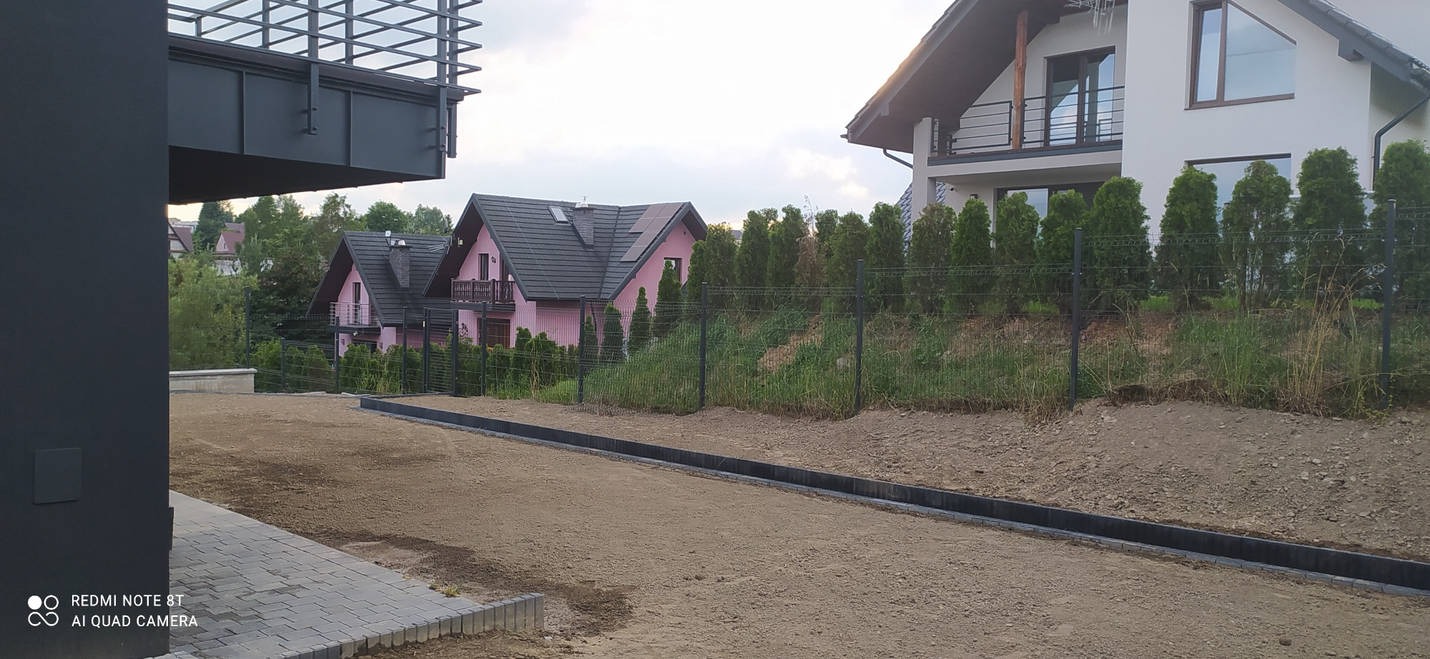 Przygotowanie terenu pod kostkę brukową z widocznymi obrzeżami i wyrównaną powierzchnią piasku, w tle domy jednorodzinne.