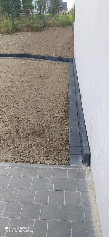 Przygotowanie terenu pod przyszłą nawierzchnię w Krakowie, z widocznymi obrzeżami z kostki betonowej i fragmentem ułożonej kostki brukowej.