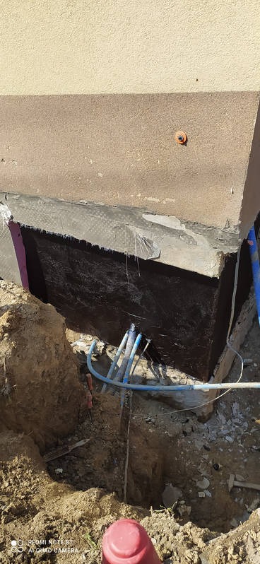 Zabezpieczony fundament budynku z widoczną hydroizolacją, wykopem i wystającymi rurami instalacyjnymi