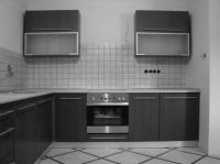 Czarno-białe zdjęcie kuchni z zabudową meblową w stylu retro, z ciemnymi szafkami wiszącymi i stojącymi, płytkami na ścianie oraz wzorzystą podłogą.
