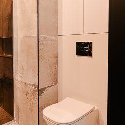 Pracownia architektoniczna Katarzyna Certa - Nowoczesna łazienka z podwieszaną toaletą, beżowymi płytkami imitującymi kamień i wzorzystą podłogą. Minimalistyczna armatura i szafka w jasnym odcieniu.