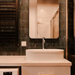 Pracownia architektoniczna Katarzyna Certa - Nowoczesna łazienka z umywalką nablatową, zieloną mozaiką na ścianie i minimalistycznym grzejnikiem drabinkowym. W tle widoczna kabina prysznicowa.