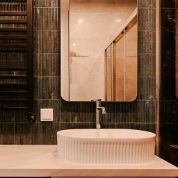 Pracownia architektoniczna Katarzyna Certa - Nowoczesna łazienka z umywalką nablatową, lustrem w metalowej ramie i grzejnikiem drabinkowym na tle płytek w odcieniach zieleni i brązu. Widoczna kabina prysznicowa.