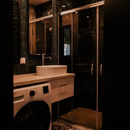 Pracownia architektoniczna Katarzyna Certa - Nowoczesna łazienka z ciemnozielonymi płytkami imitującymi marmur, kabiną prysznicową, umywalką nablatową i pralką. Wzór kwiatowy na podłodze dodaje charakteru.