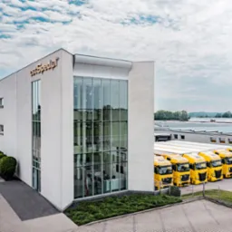 Budynek firmy transportowej z rzędem zaparkowanych, żółtych ciężarówek z logo firmy.