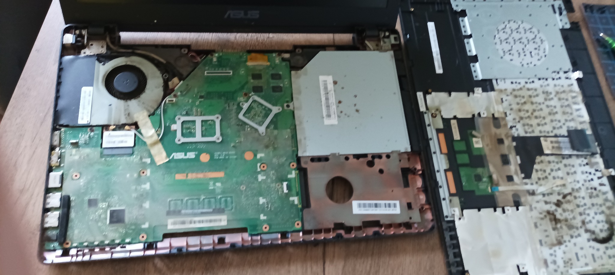 Wnętrze rozłożonego laptopa Asus z widoczną płytą główną, wentylatorem i elementami obudowy. Widoczne ślady kurzu i zabrudzeń.