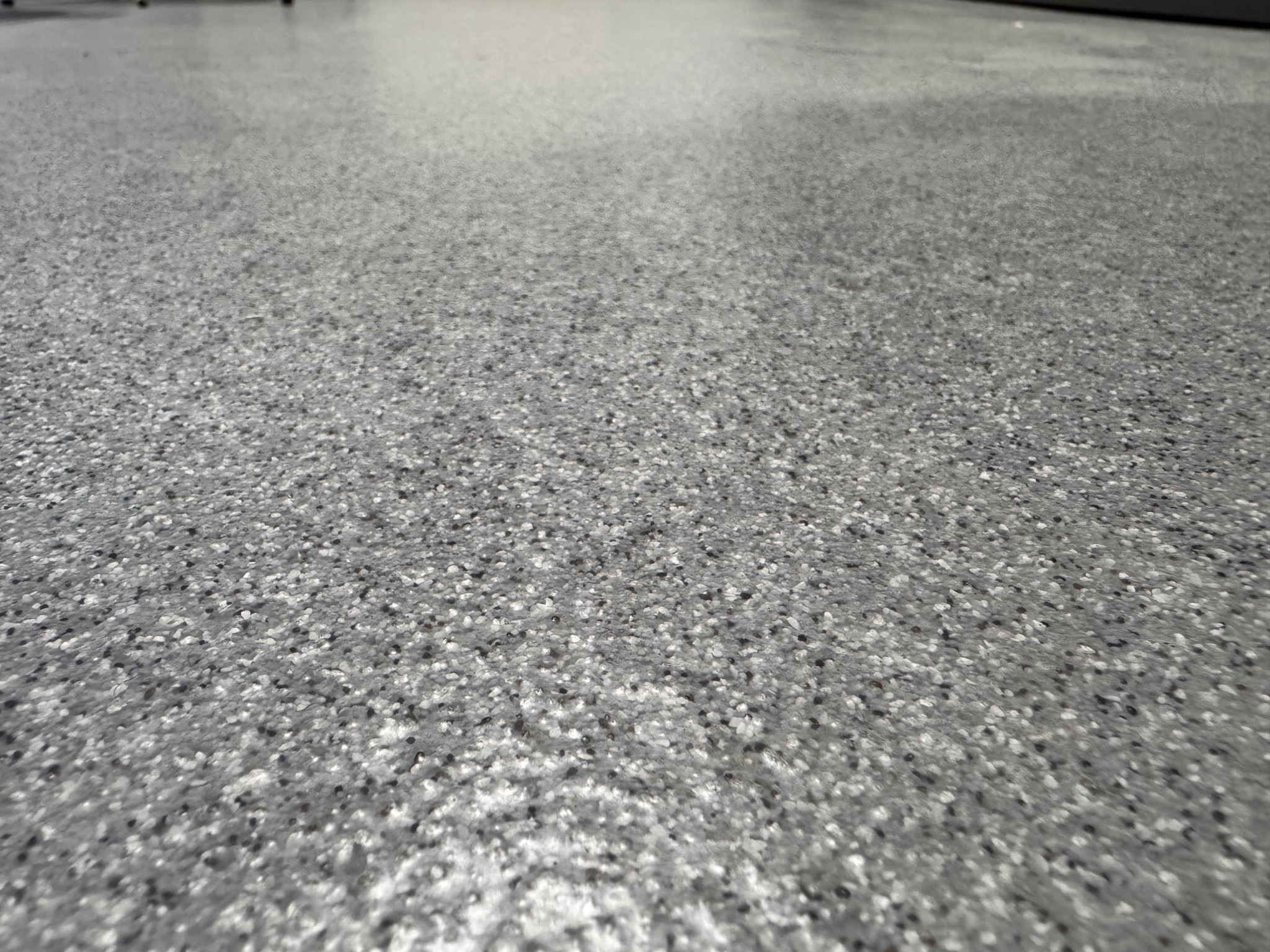 Szara, błyszcząca posadzka z drobnymi, ciemnymi i jasnymi inkluzjami, widoczna pod niskim kątem.