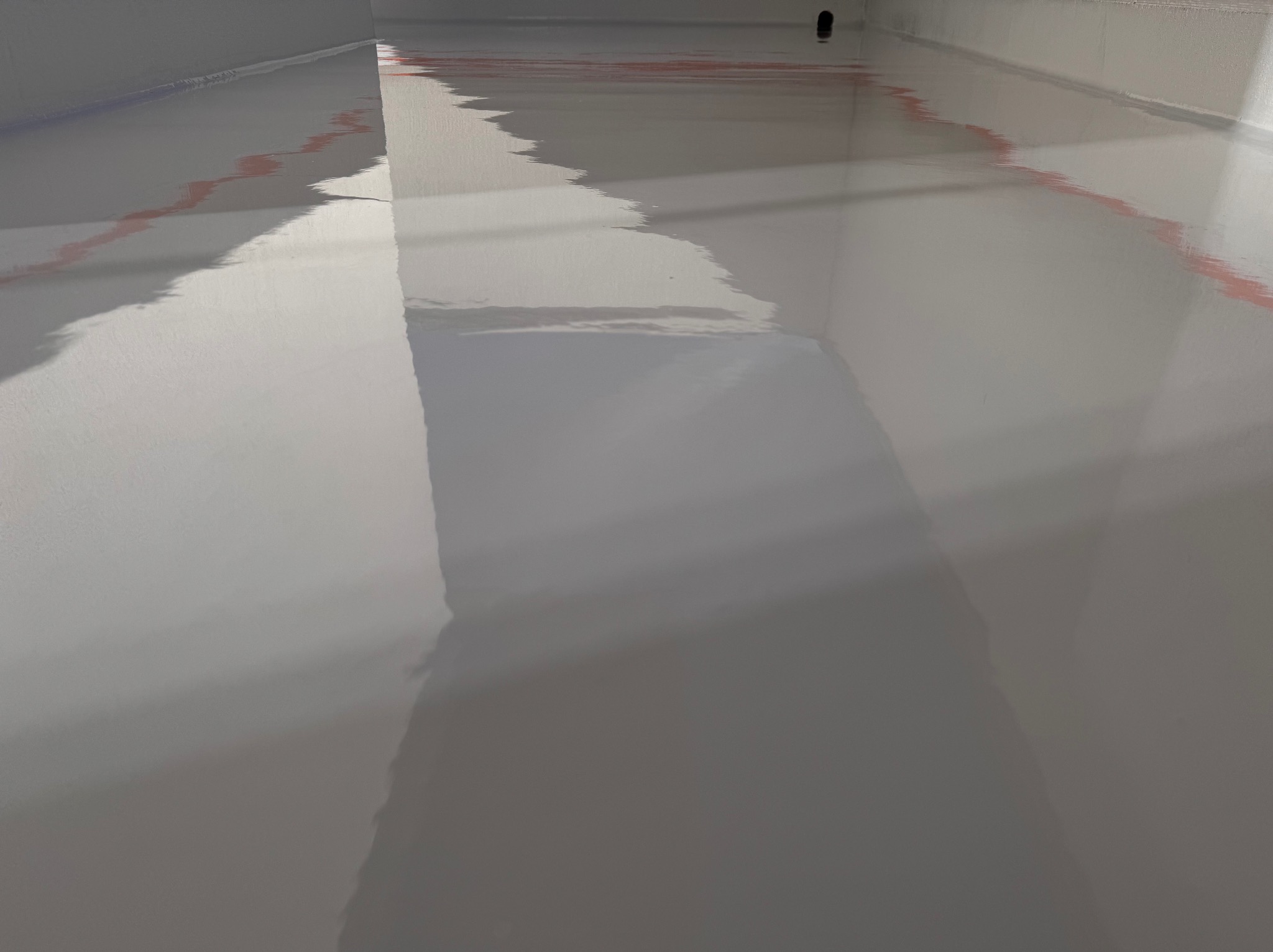 Jasnoszara, błyszcząca podłoga w pomieszczeniu, z delikatnymi, rozmazanymi refleksami czerwieni wzdłuż krawędzi ścian.